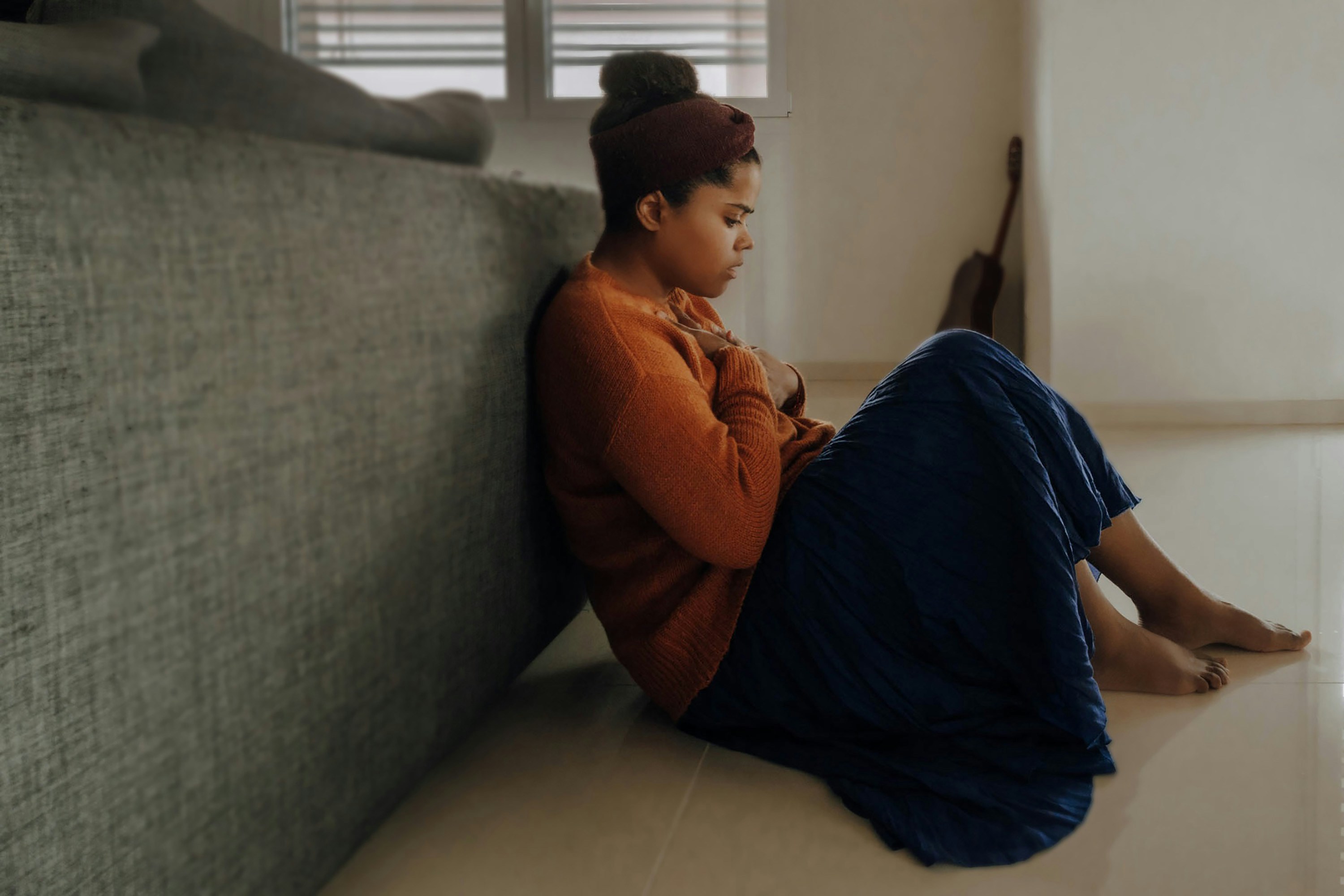 Woman sitting on the floor behind a couch with her hands on her chest, thinking about anxious attachment style.