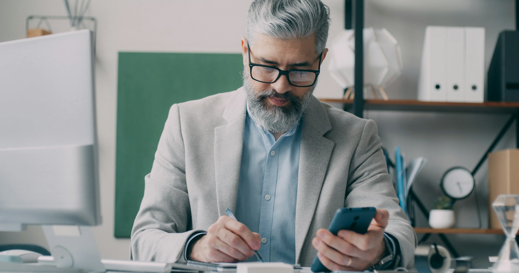 Man sitting at his desk holding a pen and phone, thinking about career dissatisfaction.