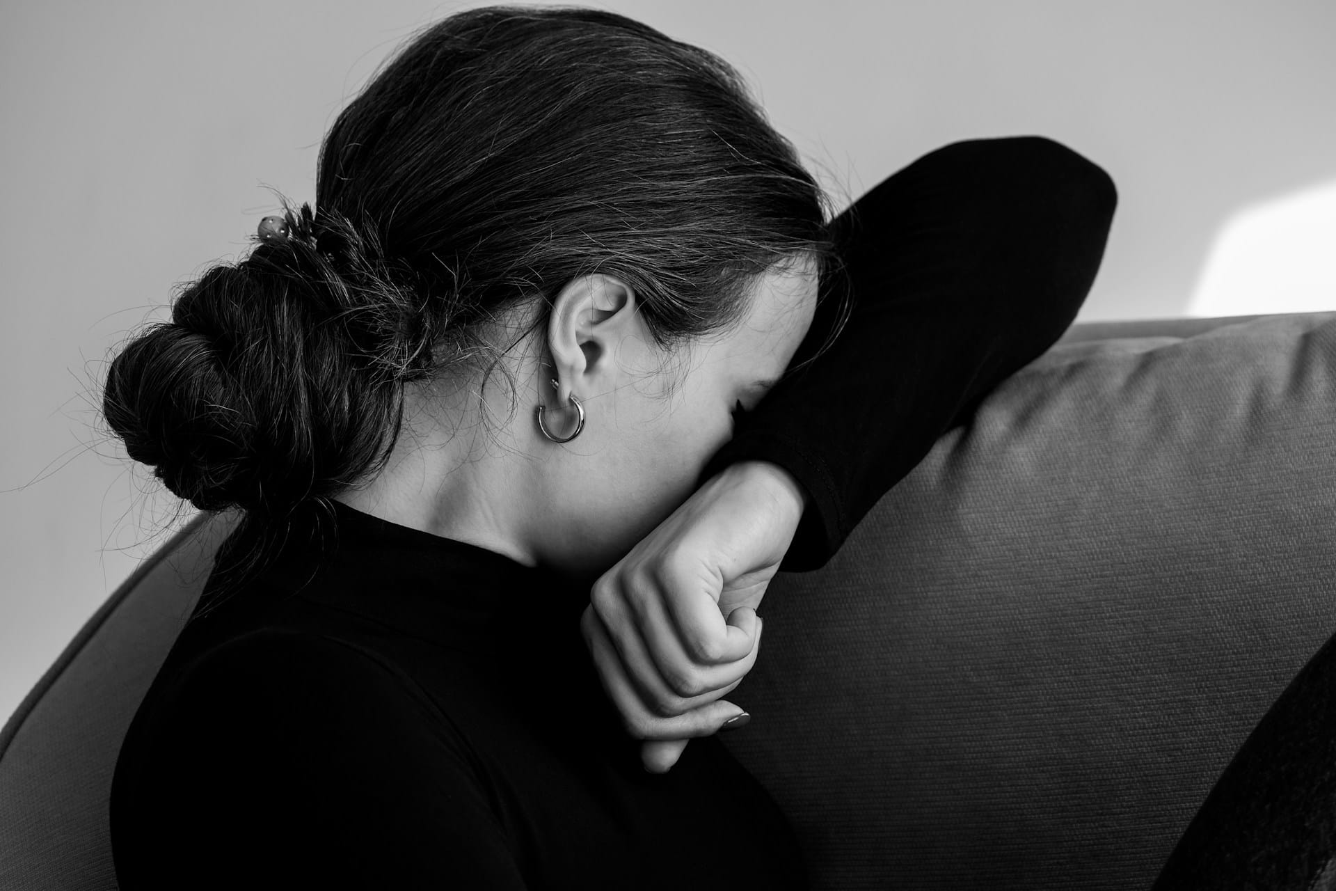 A woman sitting on a couch with her face buried in her arm, expressing grief and emotional release.