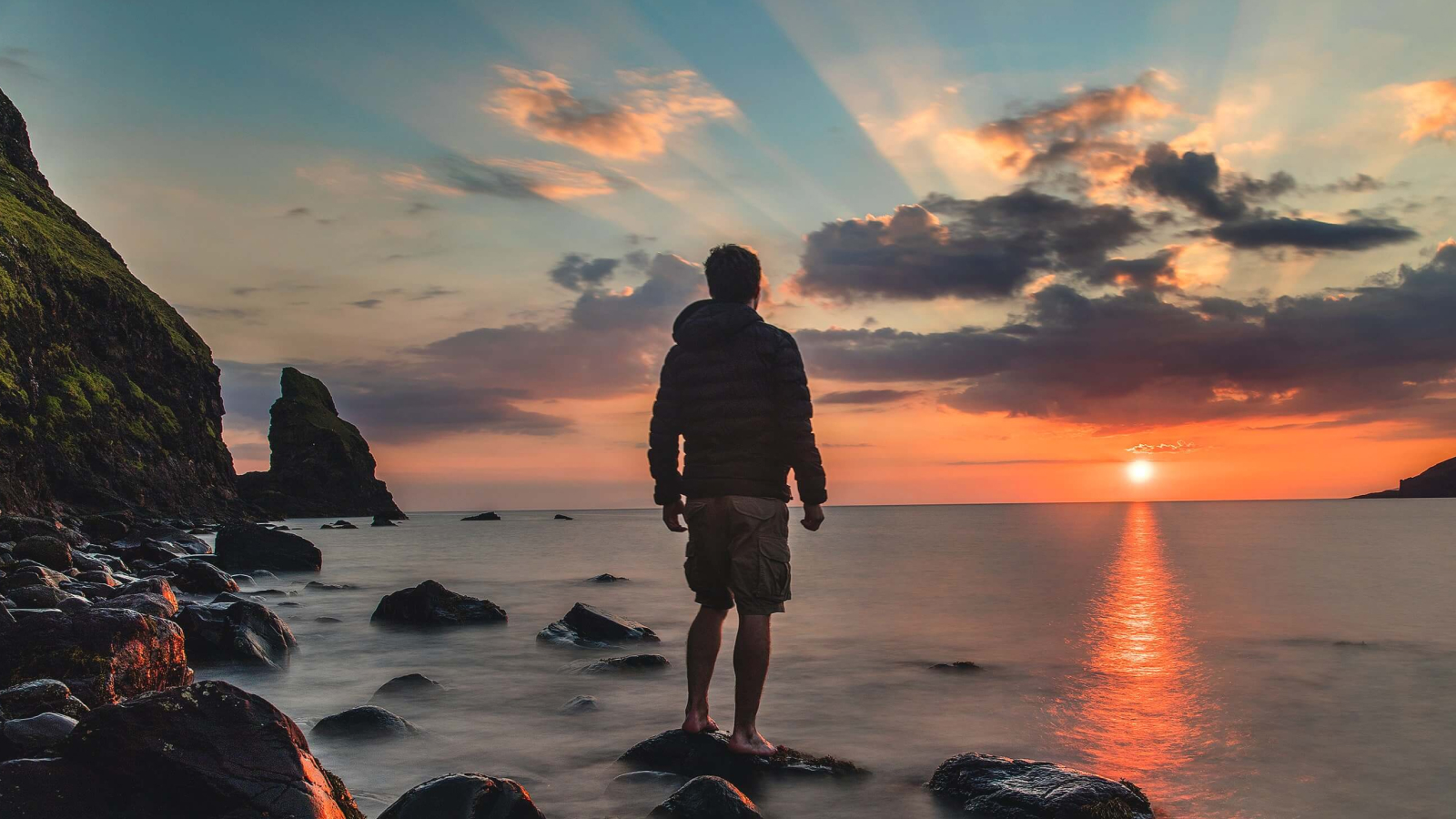 A person standing on rocks in water at sunset