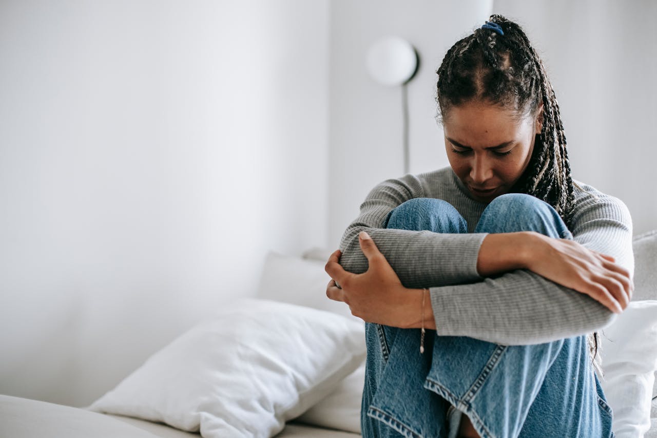 Woman sitting on her bed looking down and feeling the effects of racial microaggressions.