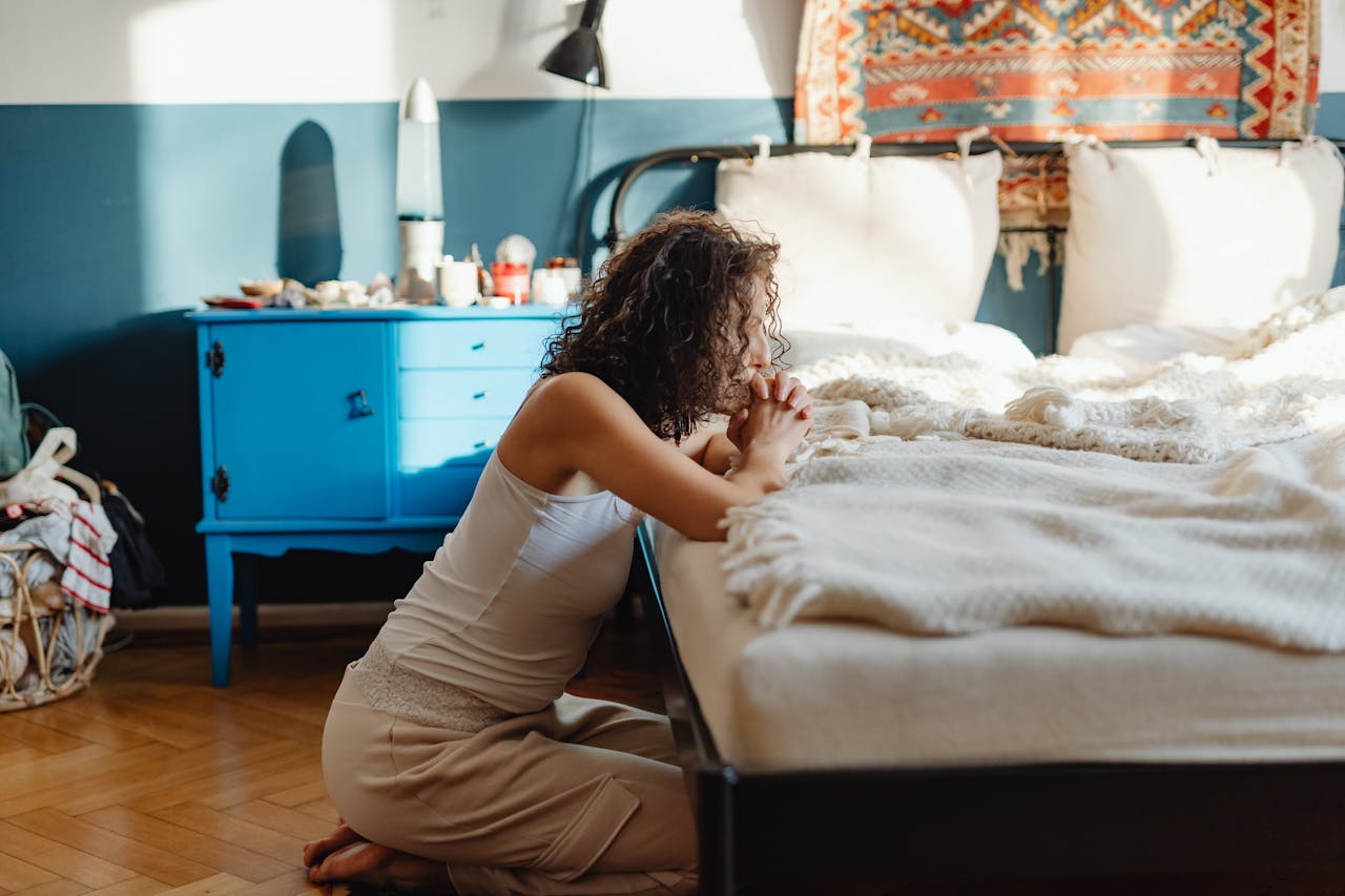 Woman in White Tank Top Praying on a Bed showing signs of religious trauma