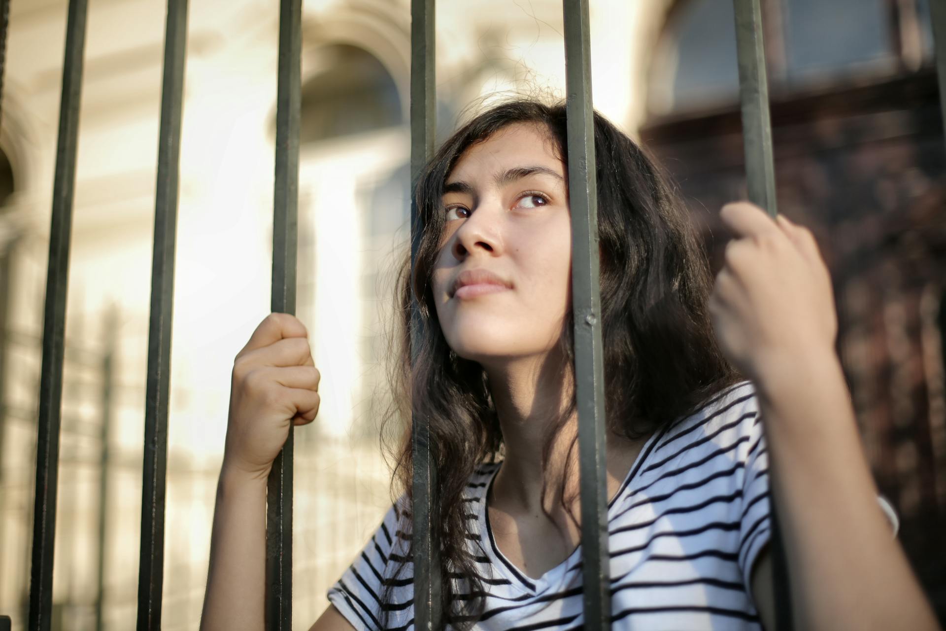 Sad isolated young woman looking away through fence with hope thinking about therapry for her religious trauma