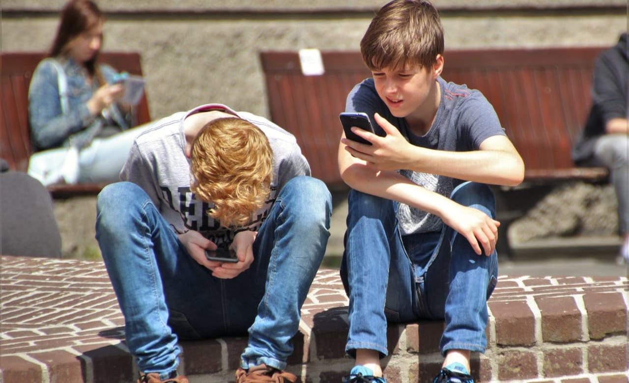 2 Boy Sitting on Brown Floor While Using Their Smartphone