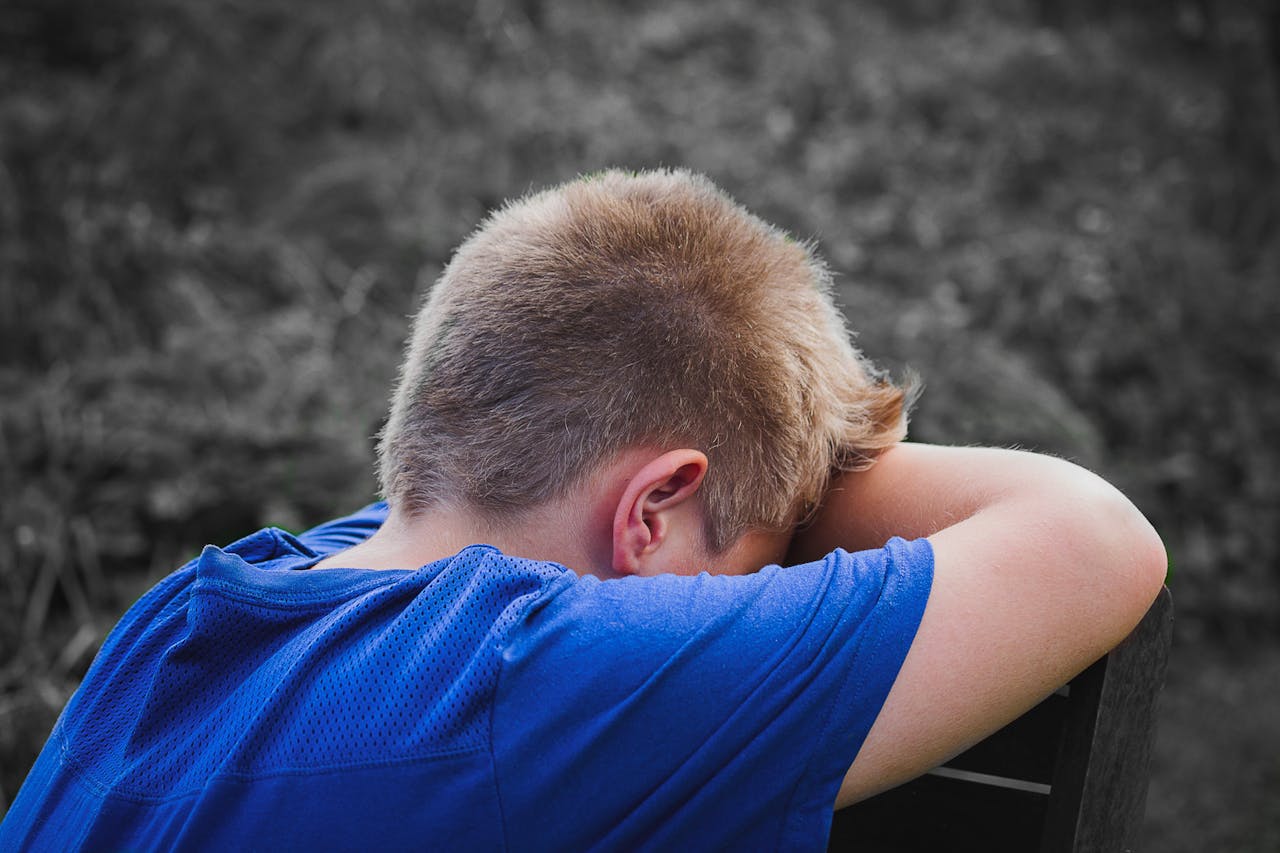 Close-up Photo of Sad Child leaning on a Wooden Chair suffering of childhood trauma