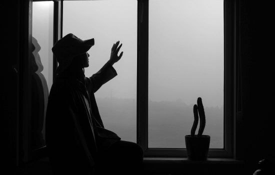silhouette of a man in a black hat looking out the window