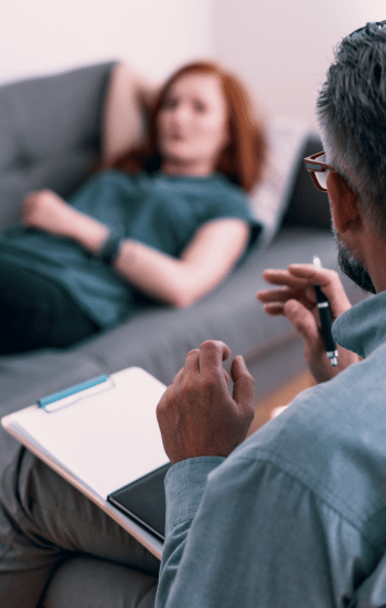 a man and woman sitting on a couch in a living room, reading a book