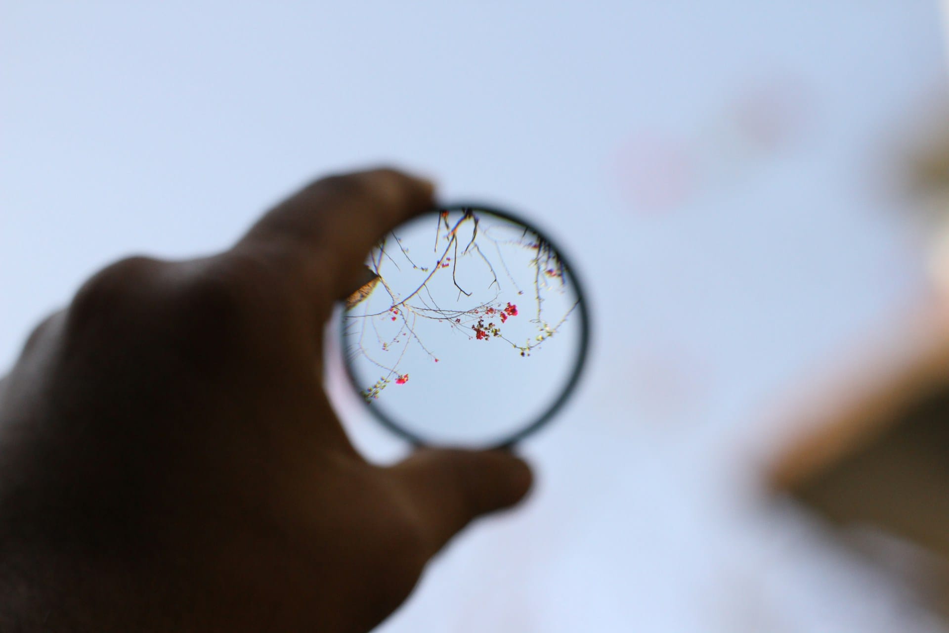 A hand holding a magnifying glass up to the sky, representative of how a mental health diagnosis can help us see and understand more.