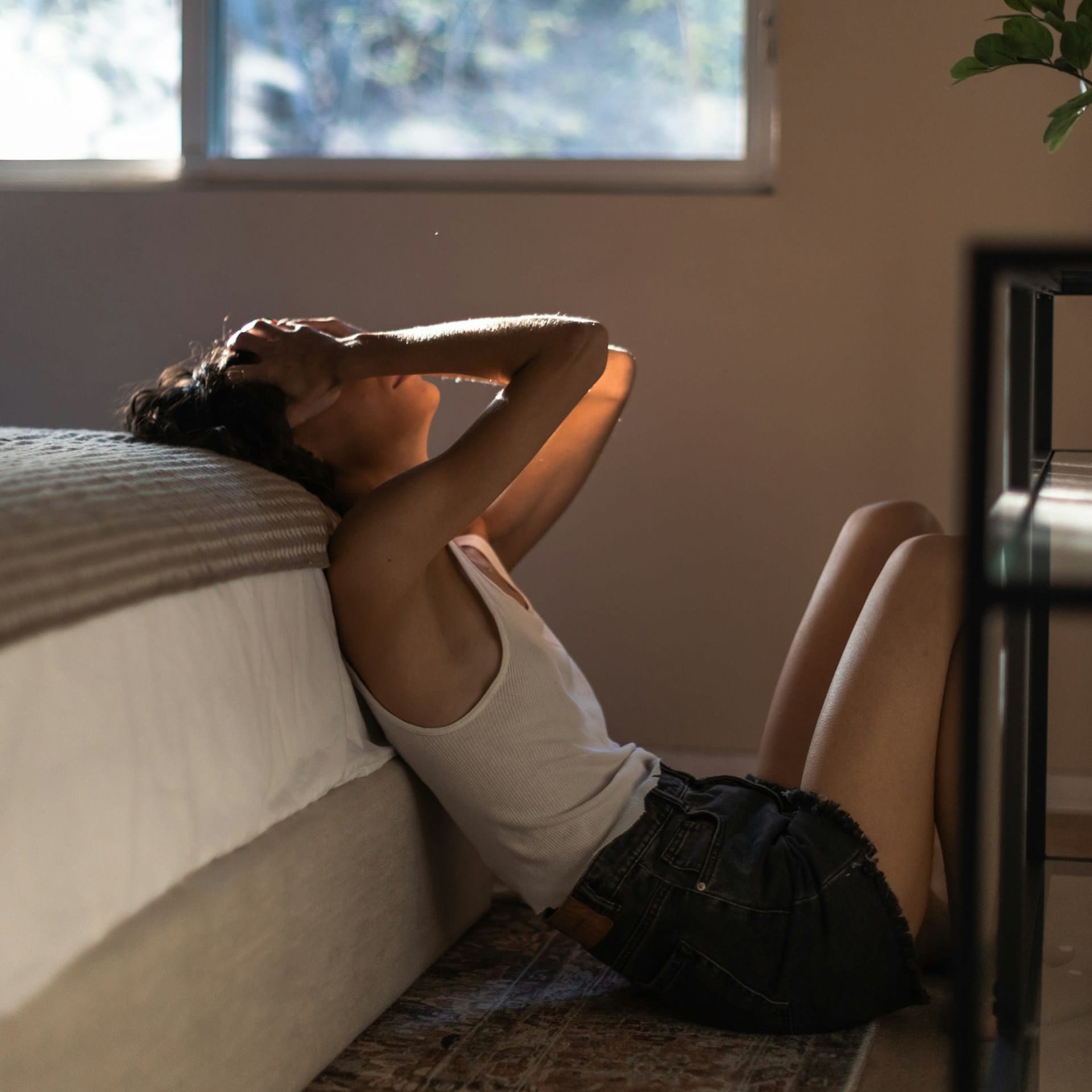 Woman sitting on the floor with her hands on her head while thinking about trauma and neurodivergence.