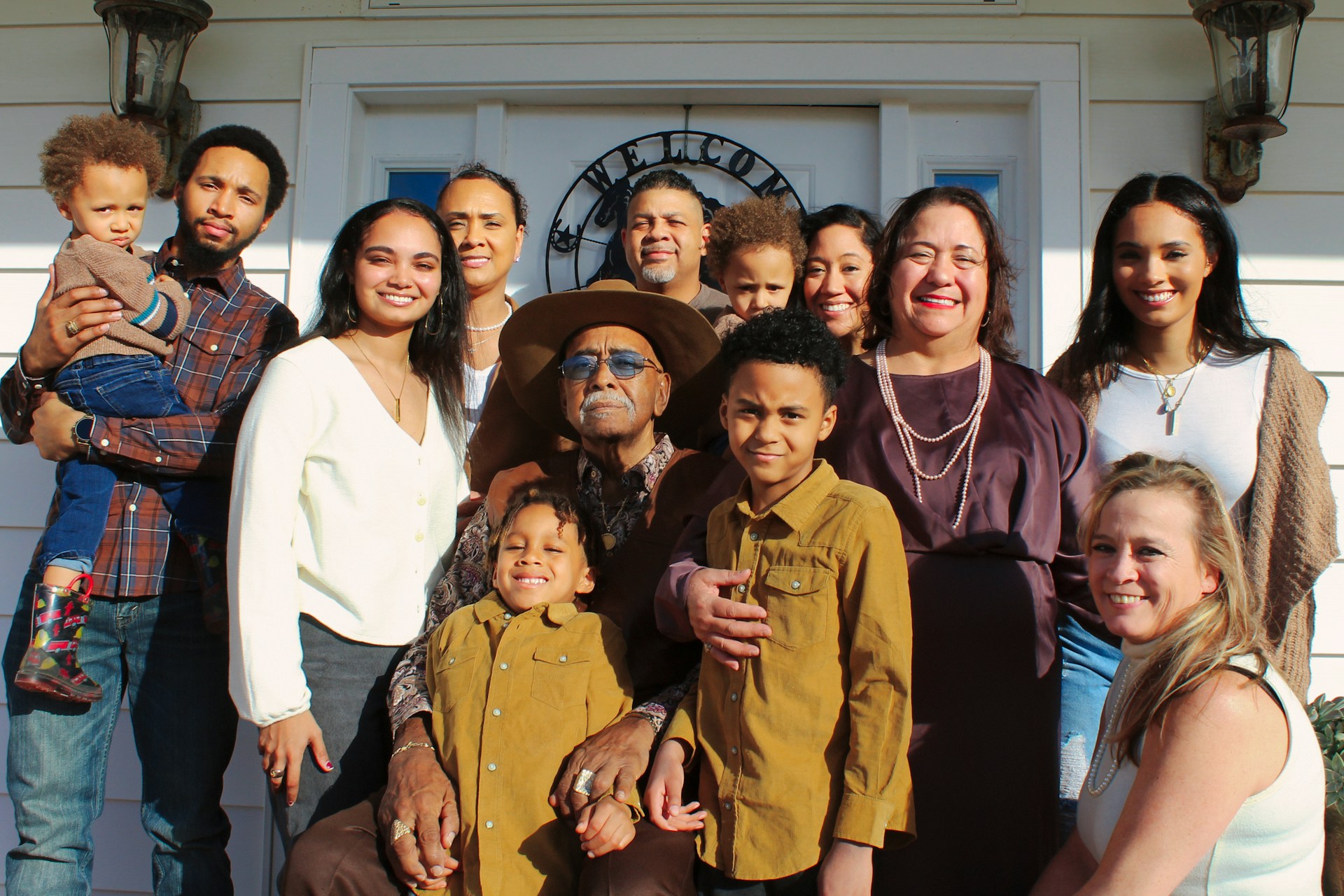 Extended family of multiple generations standing together on a front porch with the children that they help raise through shared parenting.