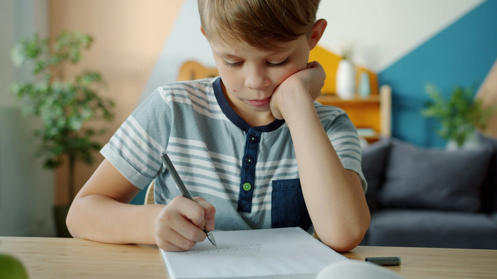Child working at a desk with their head in their hand, representative of an autistic child needing support and school accommodation regardless of a "high-functioning" autism label.