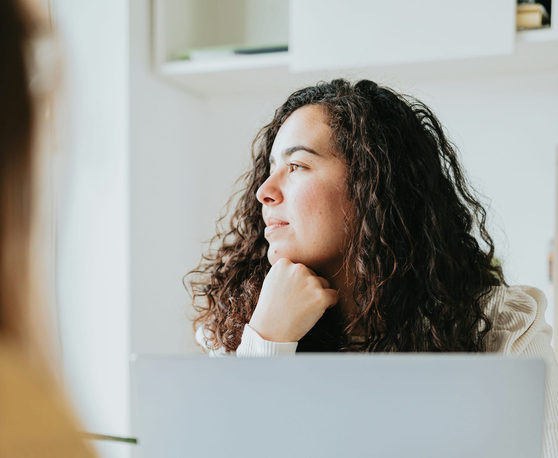 Person sitting at her laptop and staring out the window, while thinking about neurodivergent masking.