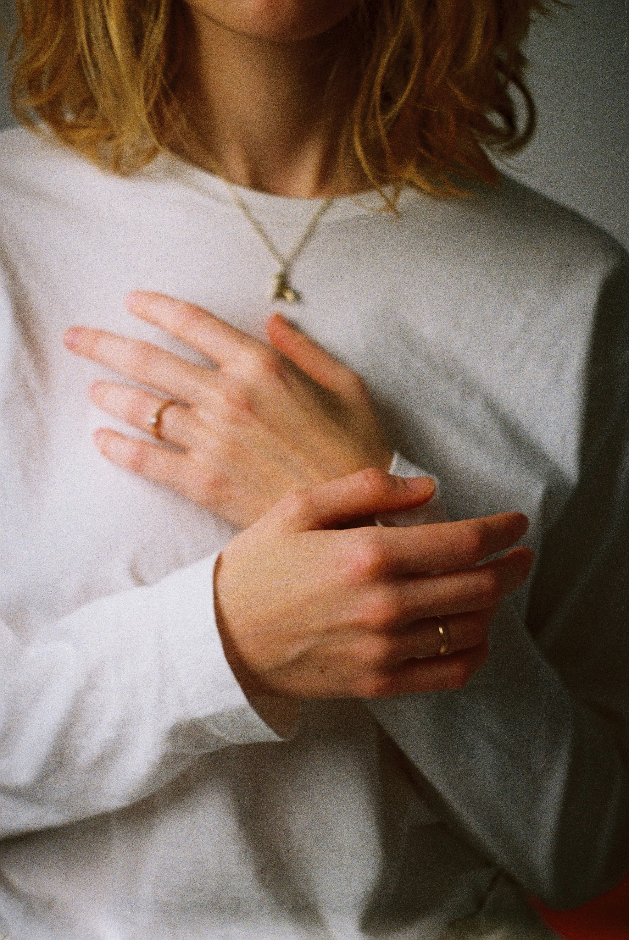 Close up of a person in a white sweater with their hands over their heart thinking about not being stuck in survival mode anymore.