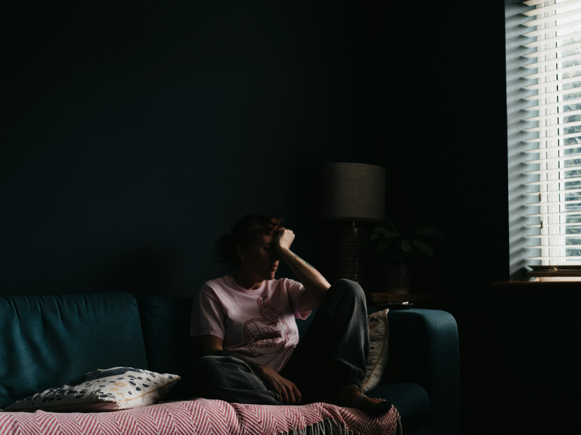 Woman sitting on a couch with her head in her hand thinking about how she is stuck in survival mode.